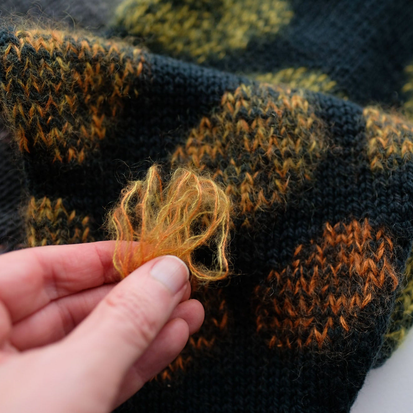 Hand holding a piece of mohair yarn against a knitted fabric background
