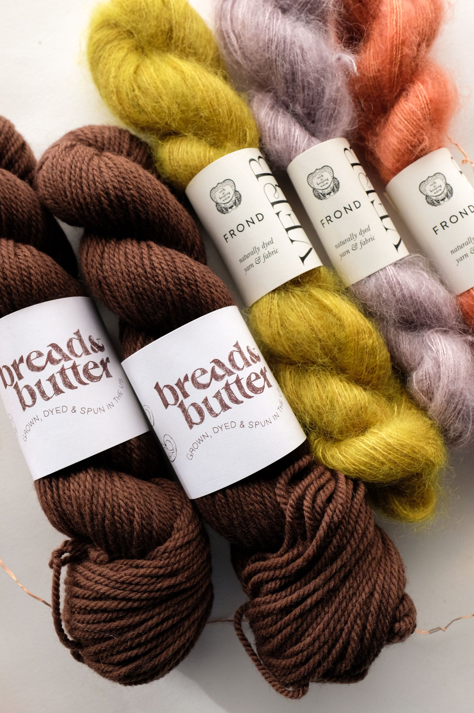 Yarn skeins in brown, yellow, lavender, and orange on a white background.