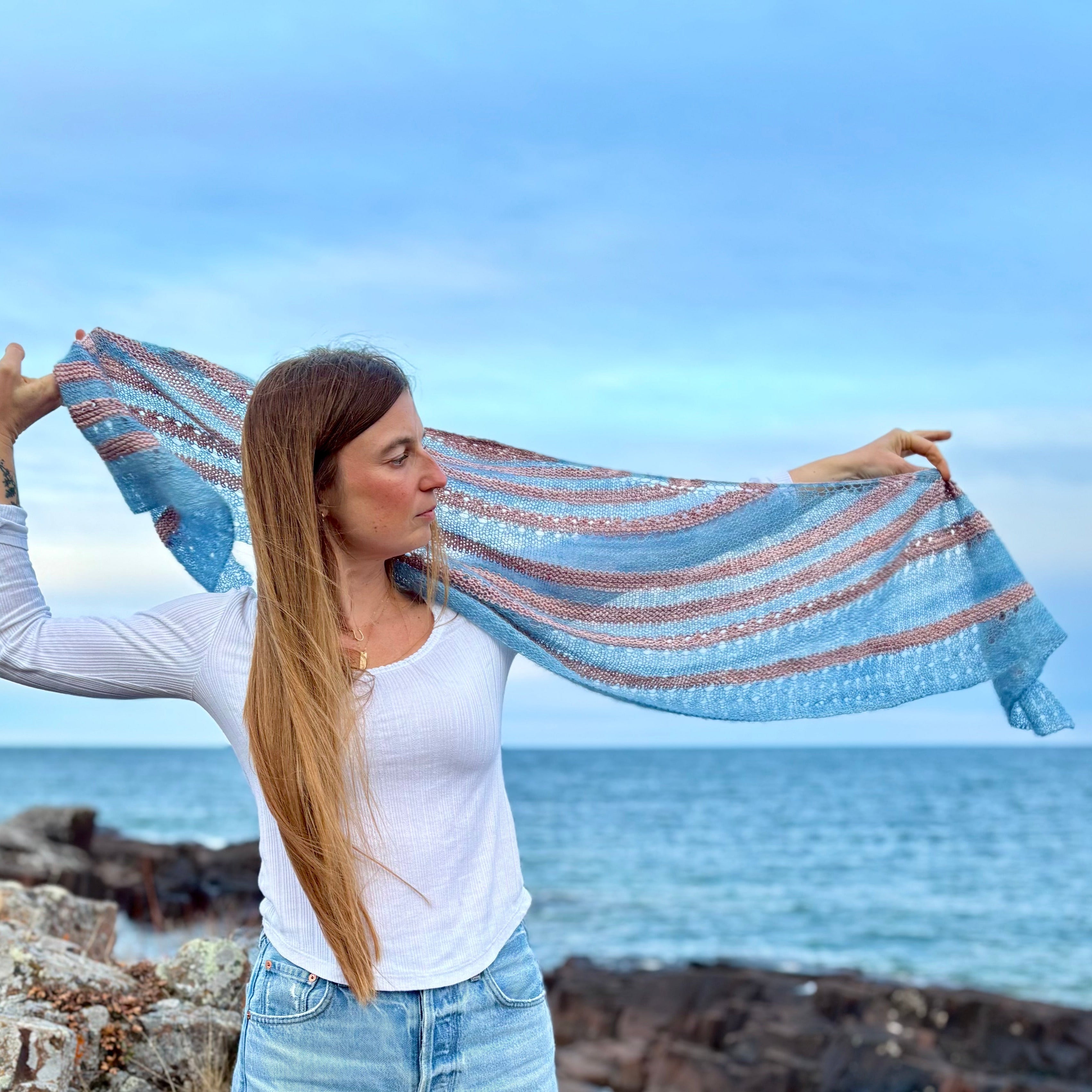 Woman holding a blue and pink striped handknit shawl by Lake Superior
