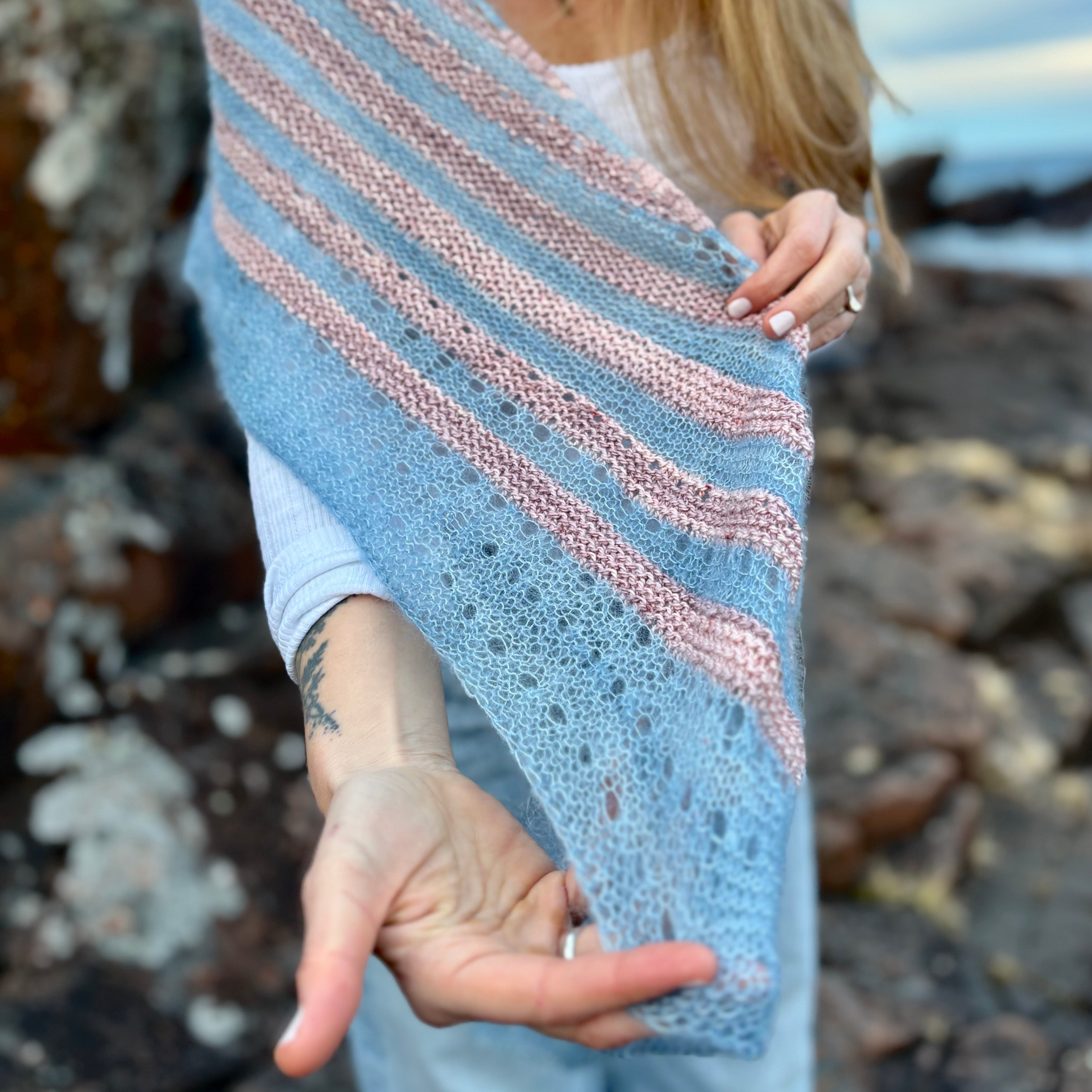 Person holding a striped knitted shawl on a rocky beach