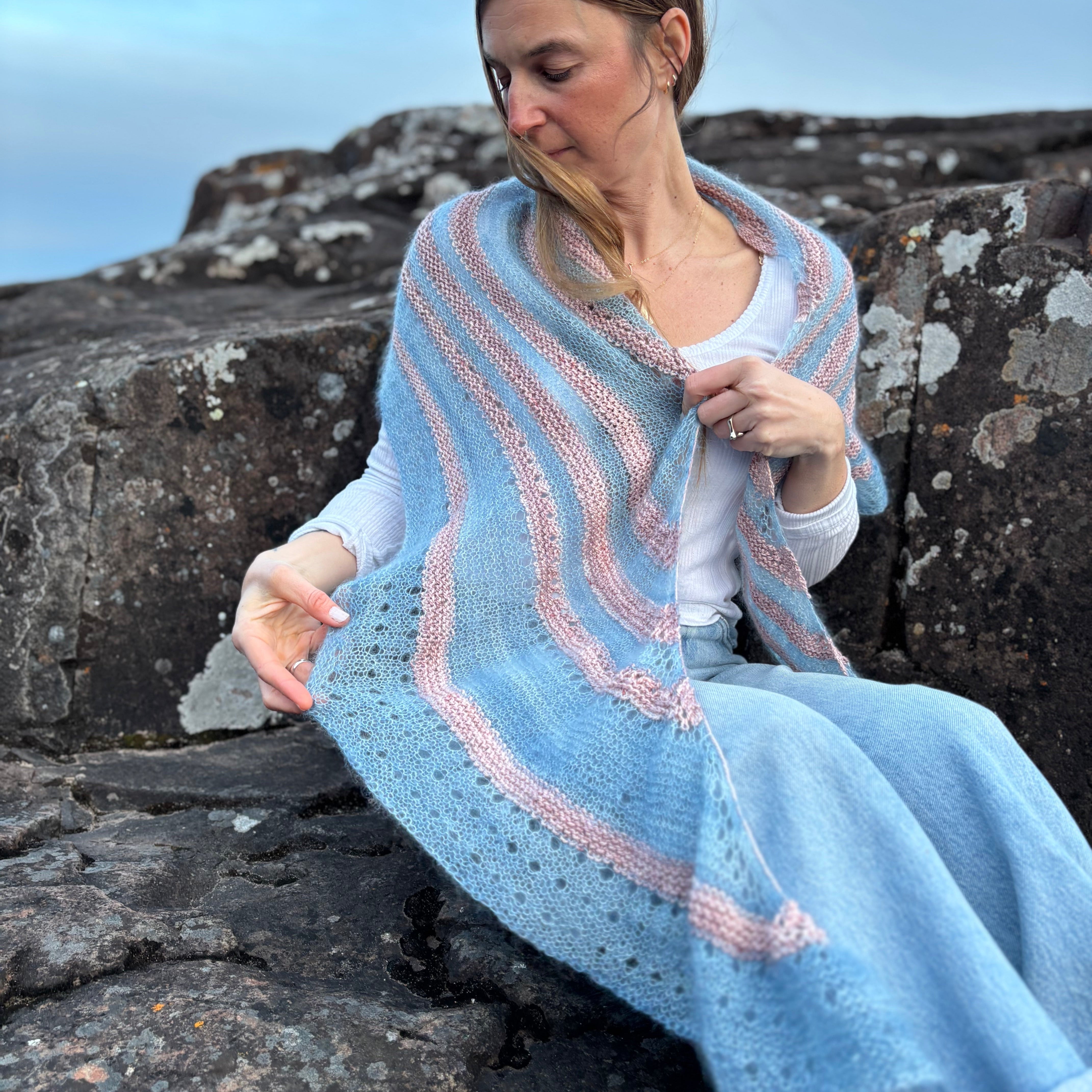 Woman sitting on rocks wearing a light blue and pink striped shawl