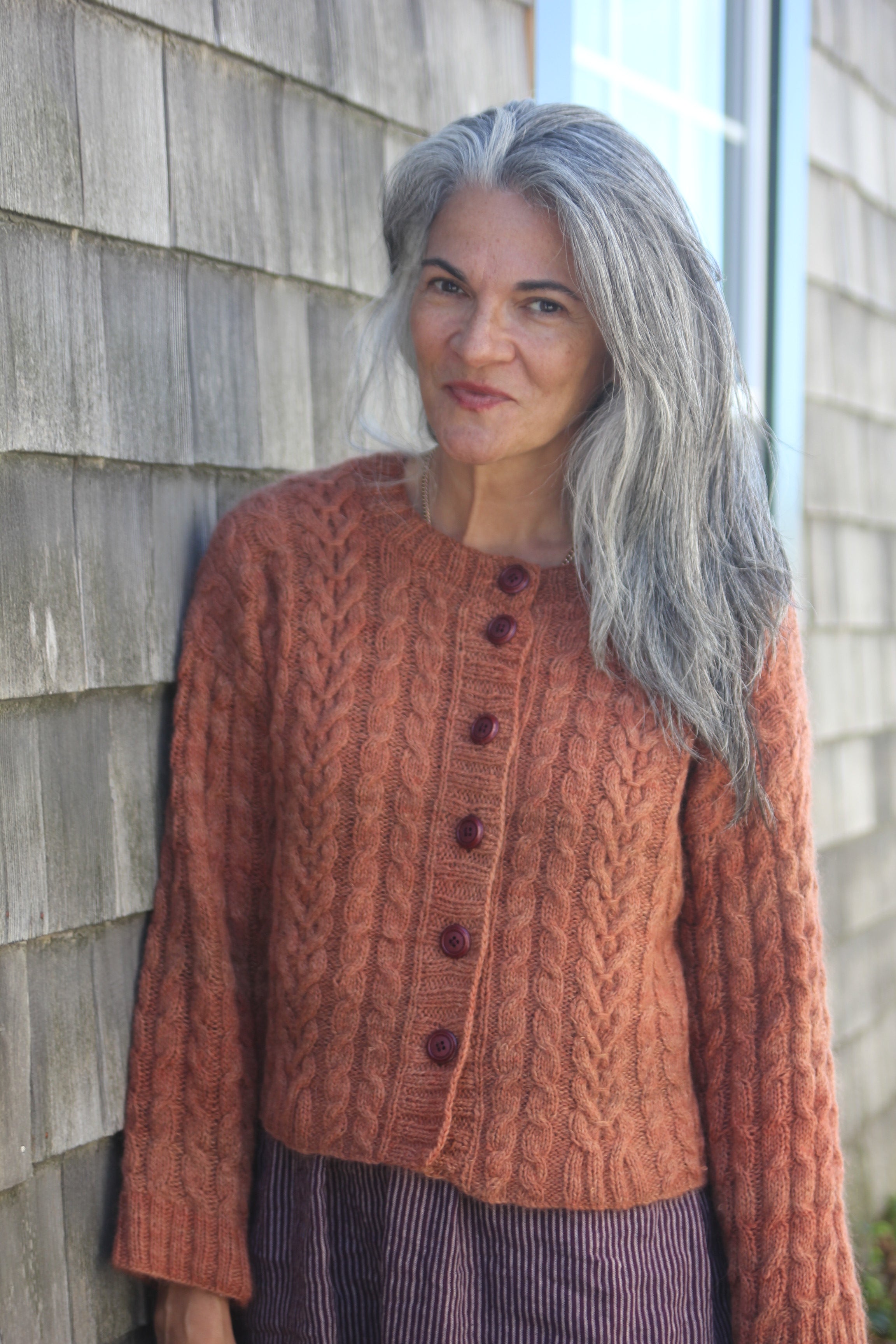 Person wearing a copper knitted cardigan with a textured wall background