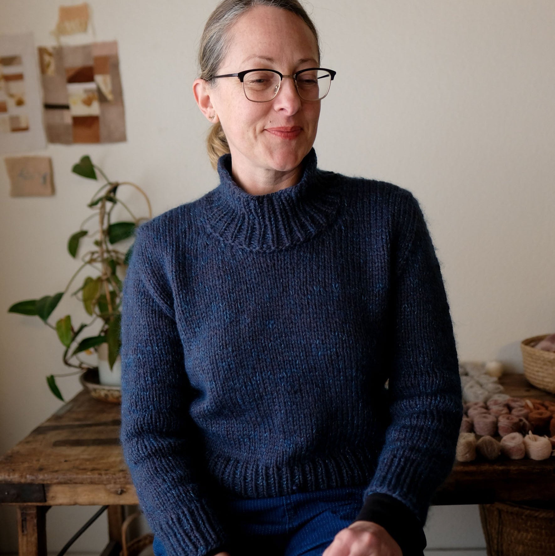 Person wearing a blue knitted sweater sitting indoors with a neutral background