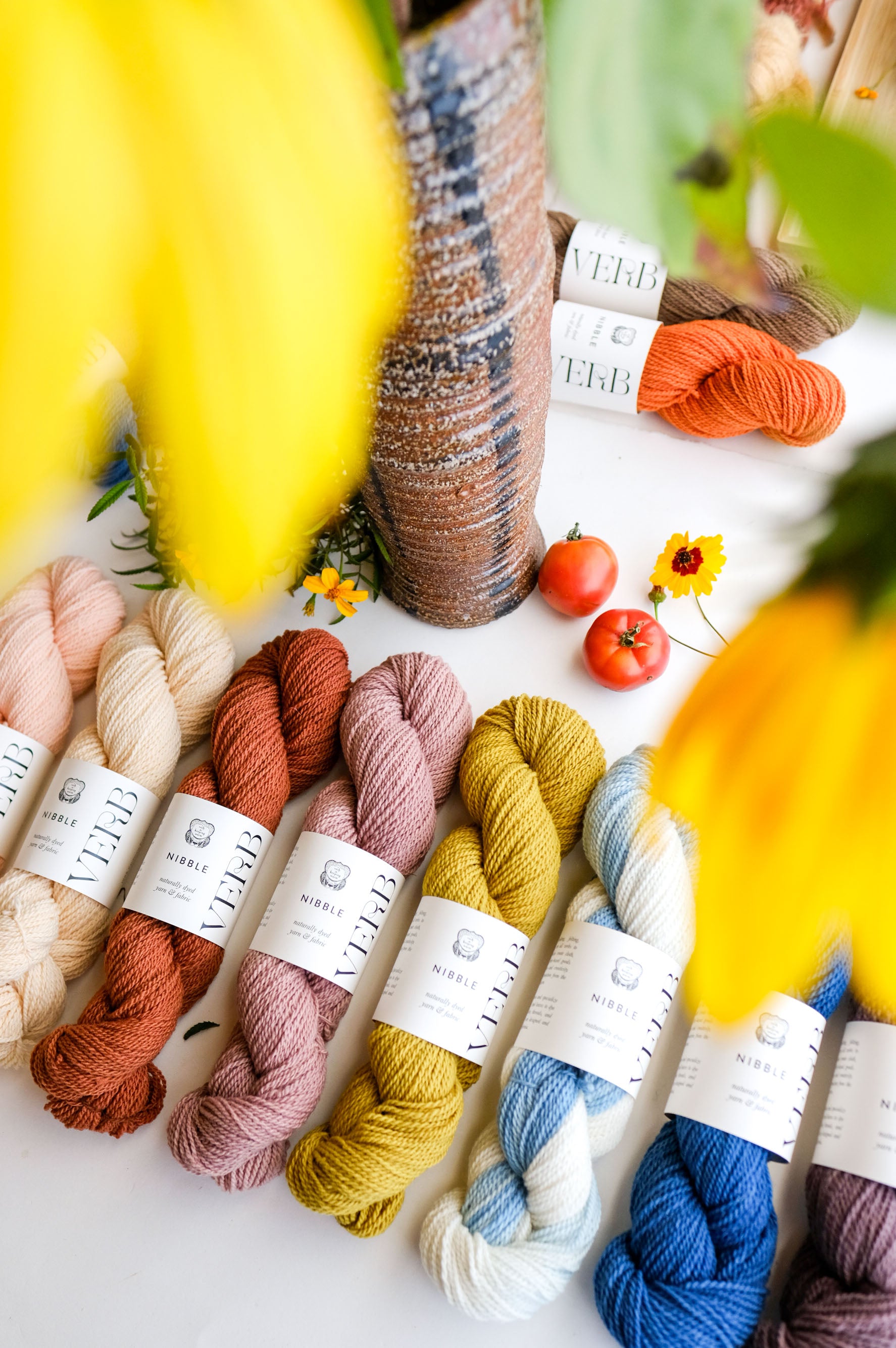 Assorted skeins of yarn in various colors with labels on a white surface, surrounded by flowers.