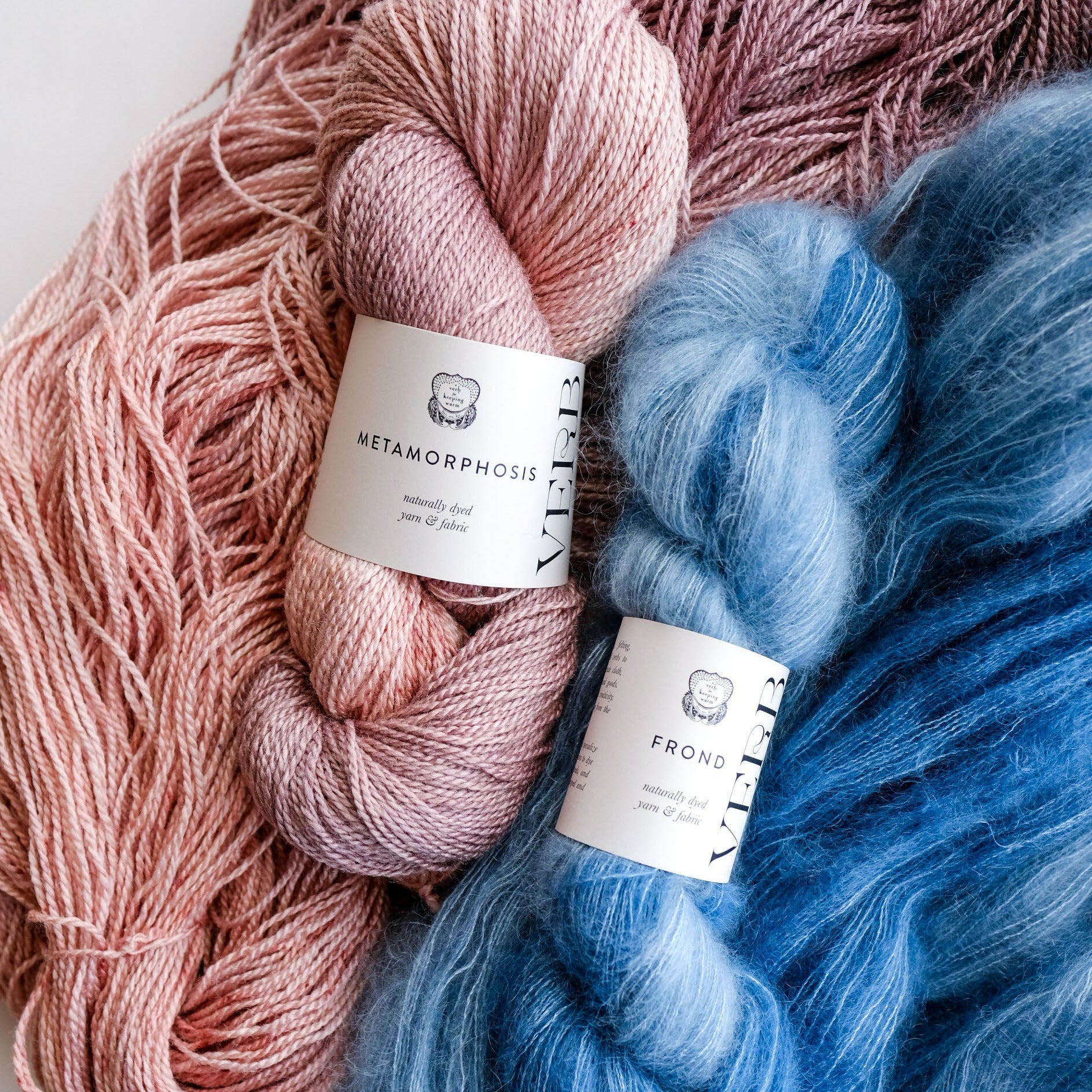 Two skeins of yarn, one pink and one blue, with labels on a white background.