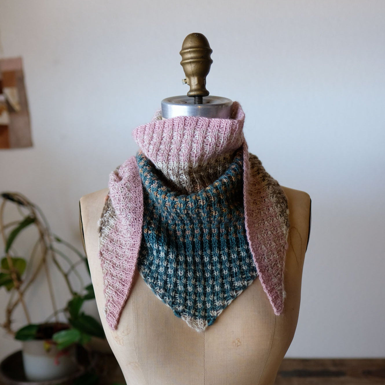 Knitted scarf on a mannequin with a wooden floor and plant in the background