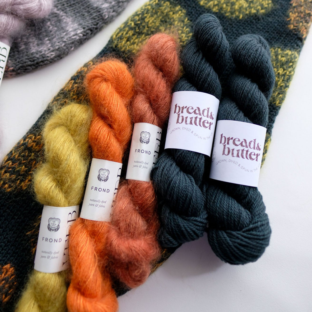 skeins of yarn in orange, green, and dark green with labels on a textured surface.