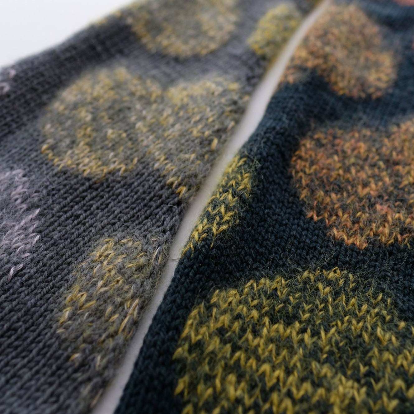 Close-up of a knitted fabric with a pattern of green and orange circles on a dark background.