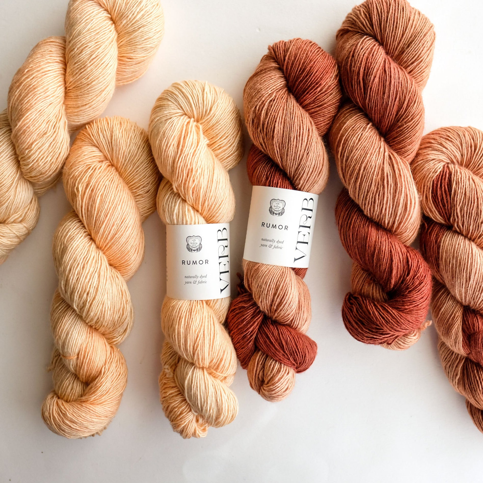 Five skeins of yarn in various shades of orange and red on a white background