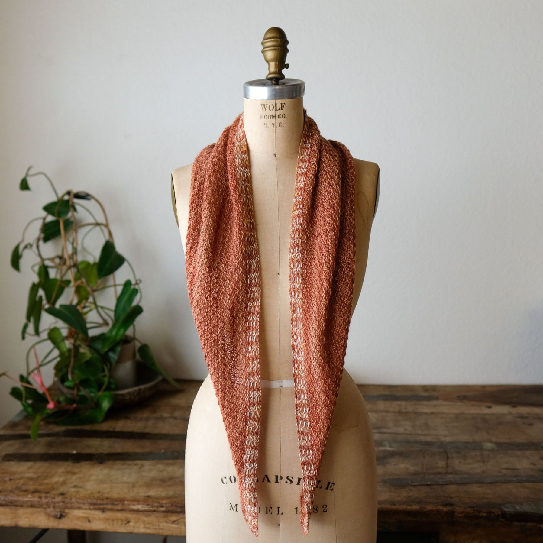 Mannequin wearing a knitted scarf with a plant and wooden table in the background