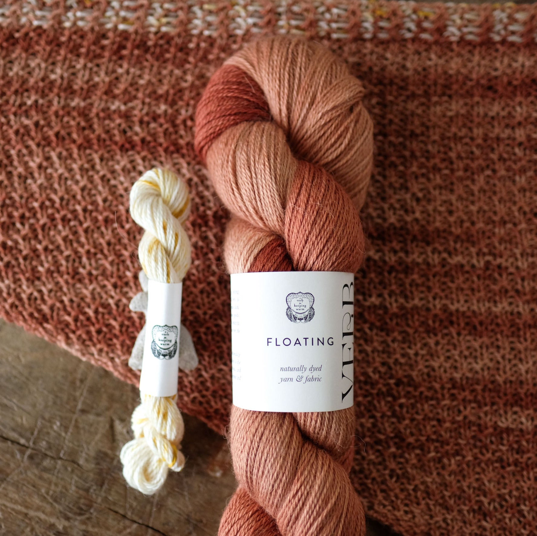 Two skeins of yarn with labels on a textured brown fabric background