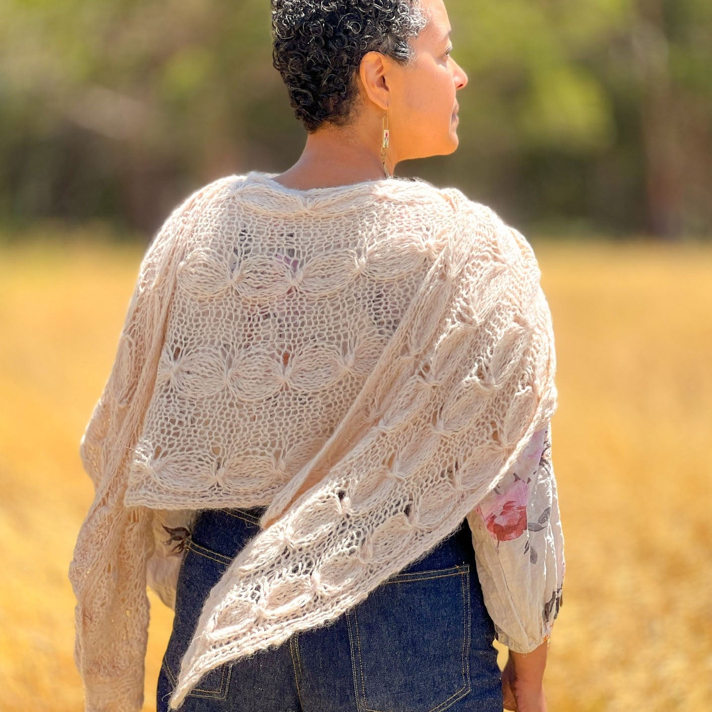 Woman wearing a handknit cable peach shawl in a field